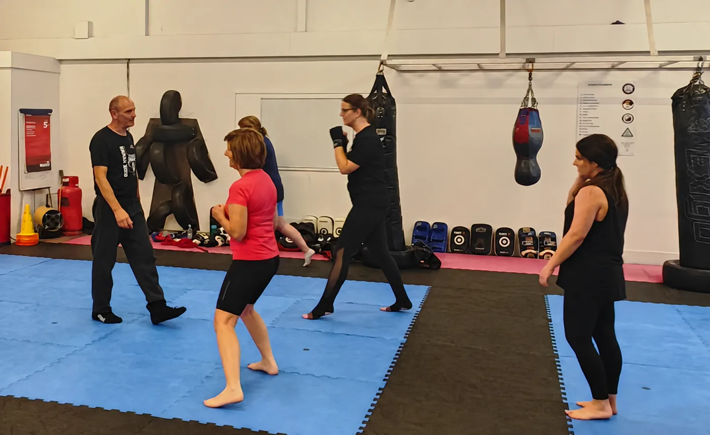 John coaching women through stance and movement practice on the academy mats