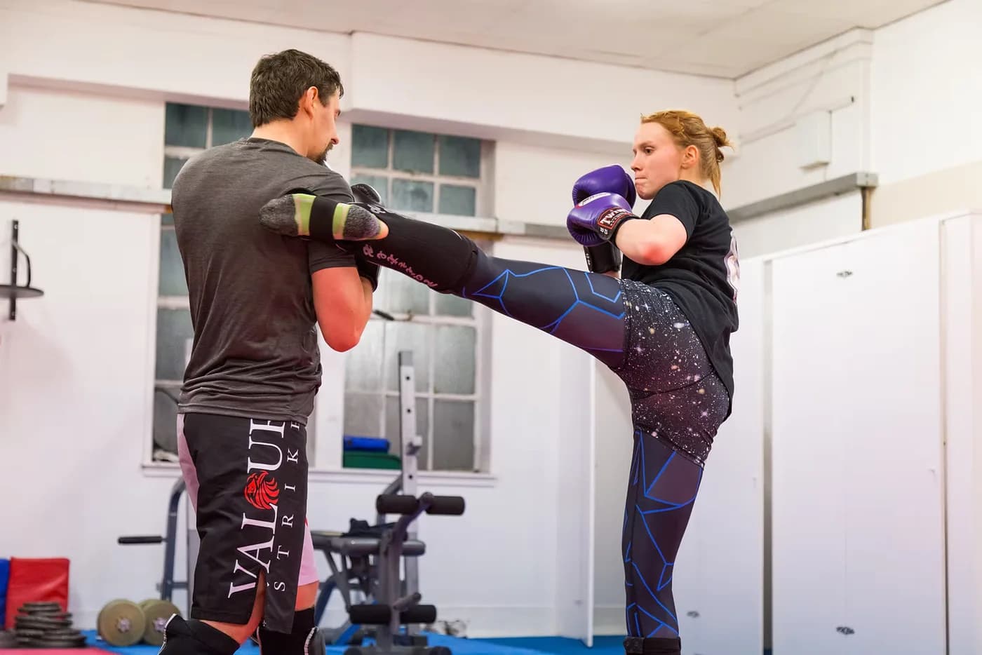 A woman practising a controlled kick with a coach holding a pad